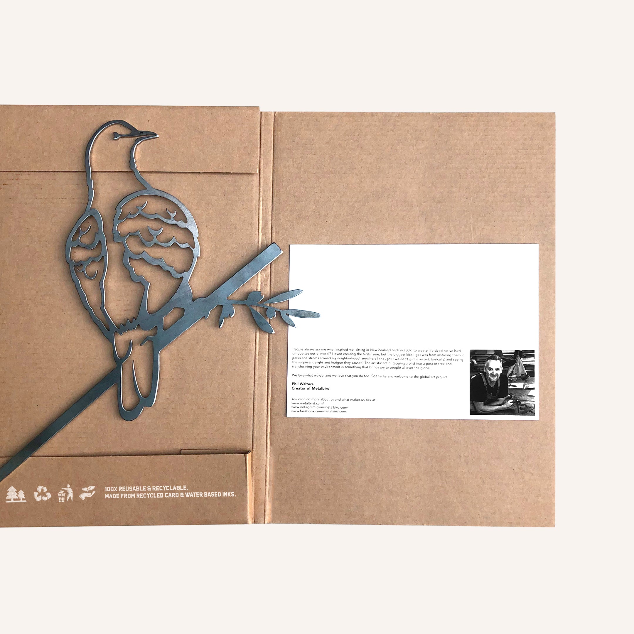 A "Turtle Dove" by Metalbird Canada perches on a brown cardboard folder holding a white card with typed text and a black-and-white photo of a person and cat, plus eco-friendly symbols printed underneath.