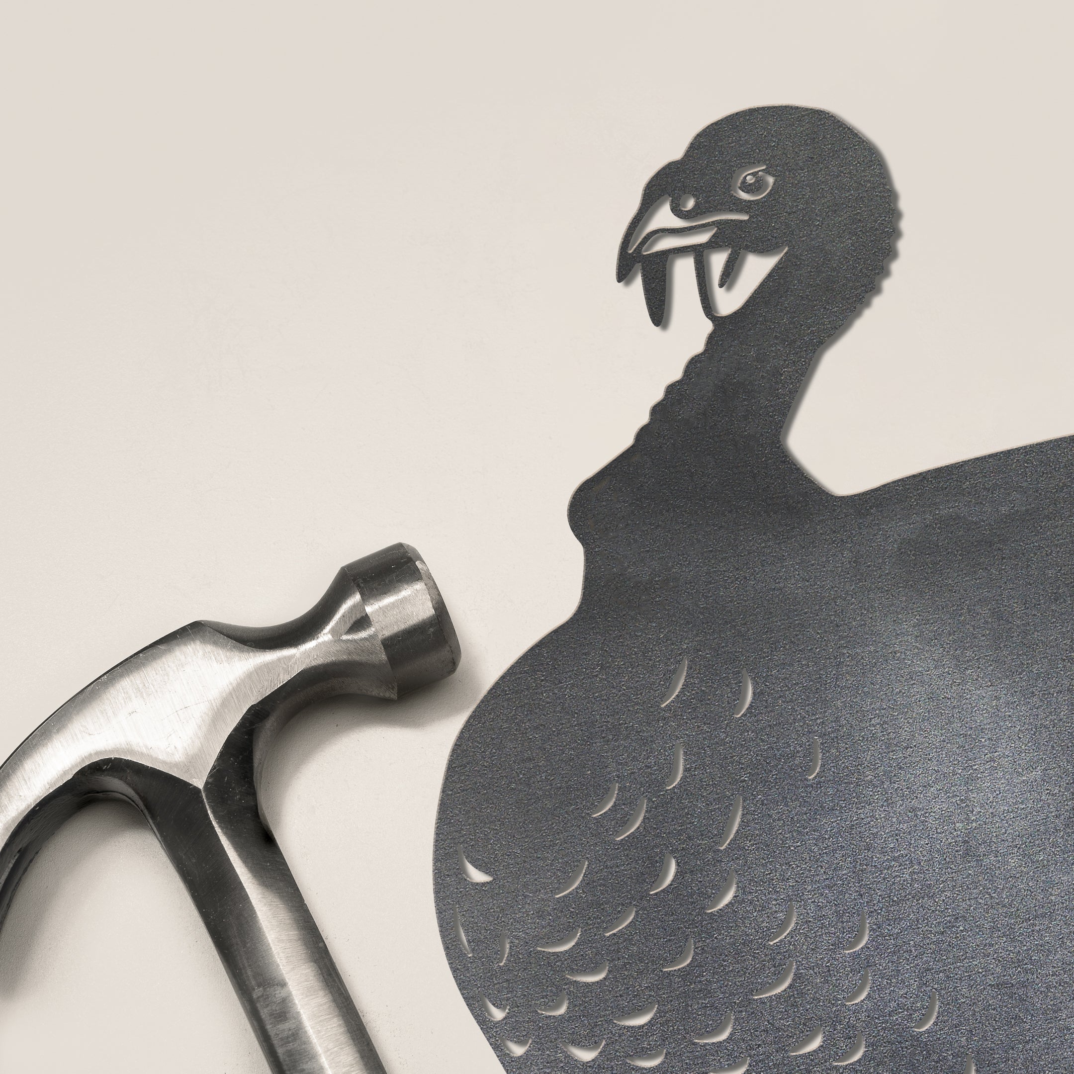A metal hammer rests on a light background, casting a shadow that resembles the Metalbird Canada Turkey, with feathered detail and a hooked beak—evoking striking metal yard art.