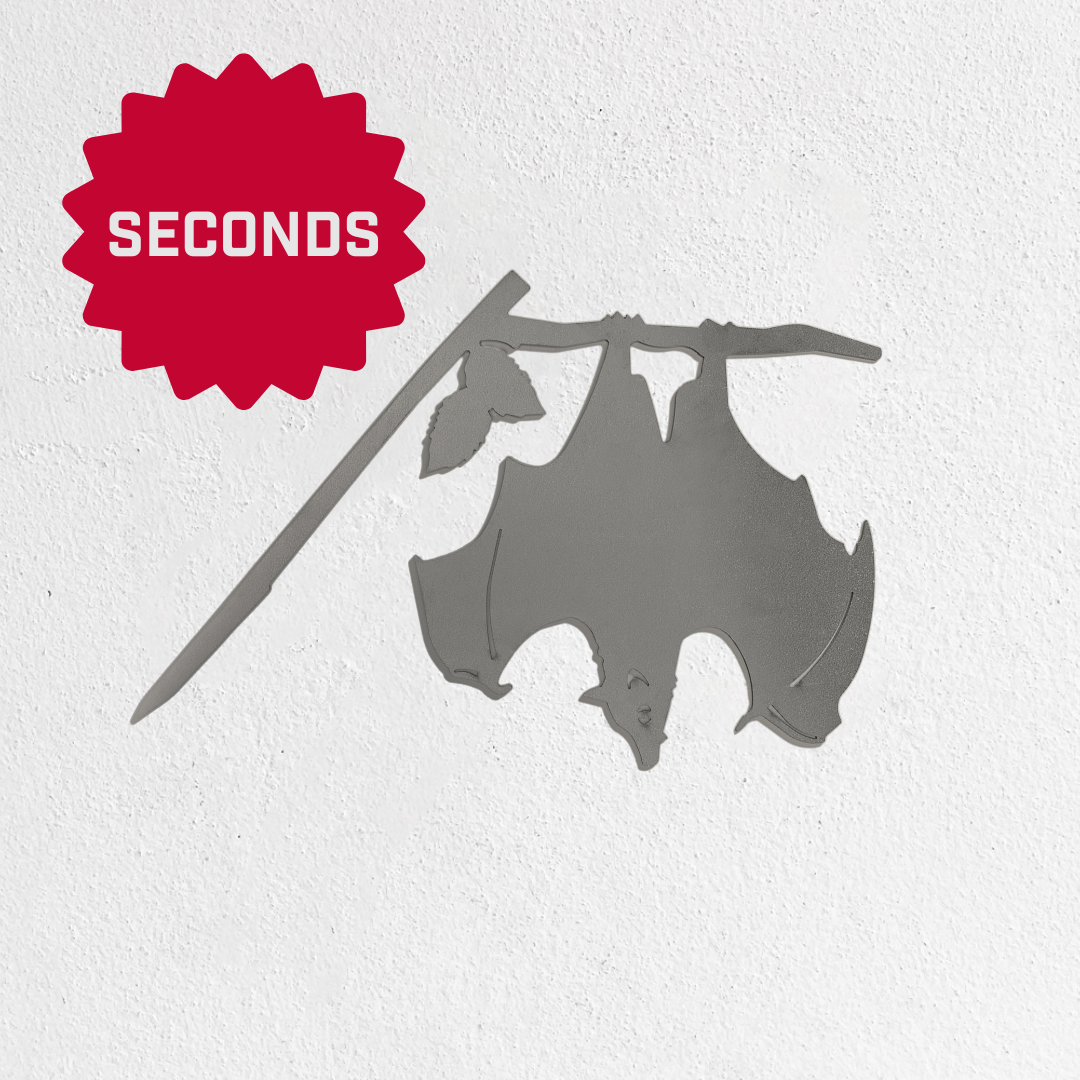The Metalbird Seconds by Metalbird Canada - Seconds features a metal bat silhouette hanging upside down from a branch against a white wall, with a red starburst labeled "SECONDS" in bold white letters—an eye-catching gift idea.
