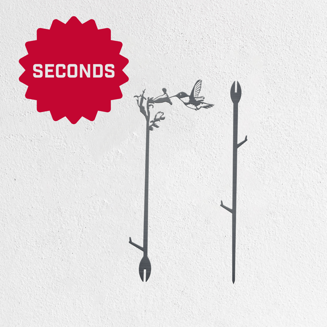 Two Metalbird Seconds garden stakes by Metalbird Canada - Seconds, each shaped like a branch with hummingbird and flower silhouettes, are shown against a white background with a red SECONDS starburst label in the top left corner.