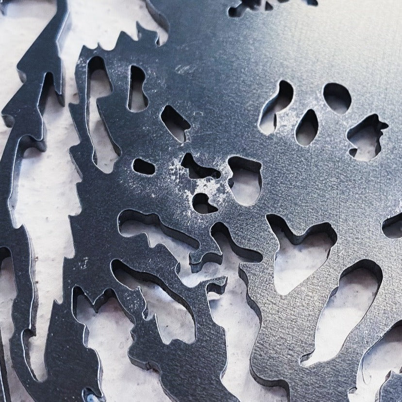 A close-up of the Metalbird Seconds by Metalbird Canada - Seconds, featuring intricate abstract cut-outs in a shiny metallic sheet. Ideal as distinctive garden or yard art, it has smooth finish and sharp edges, displayed on a light textured background.