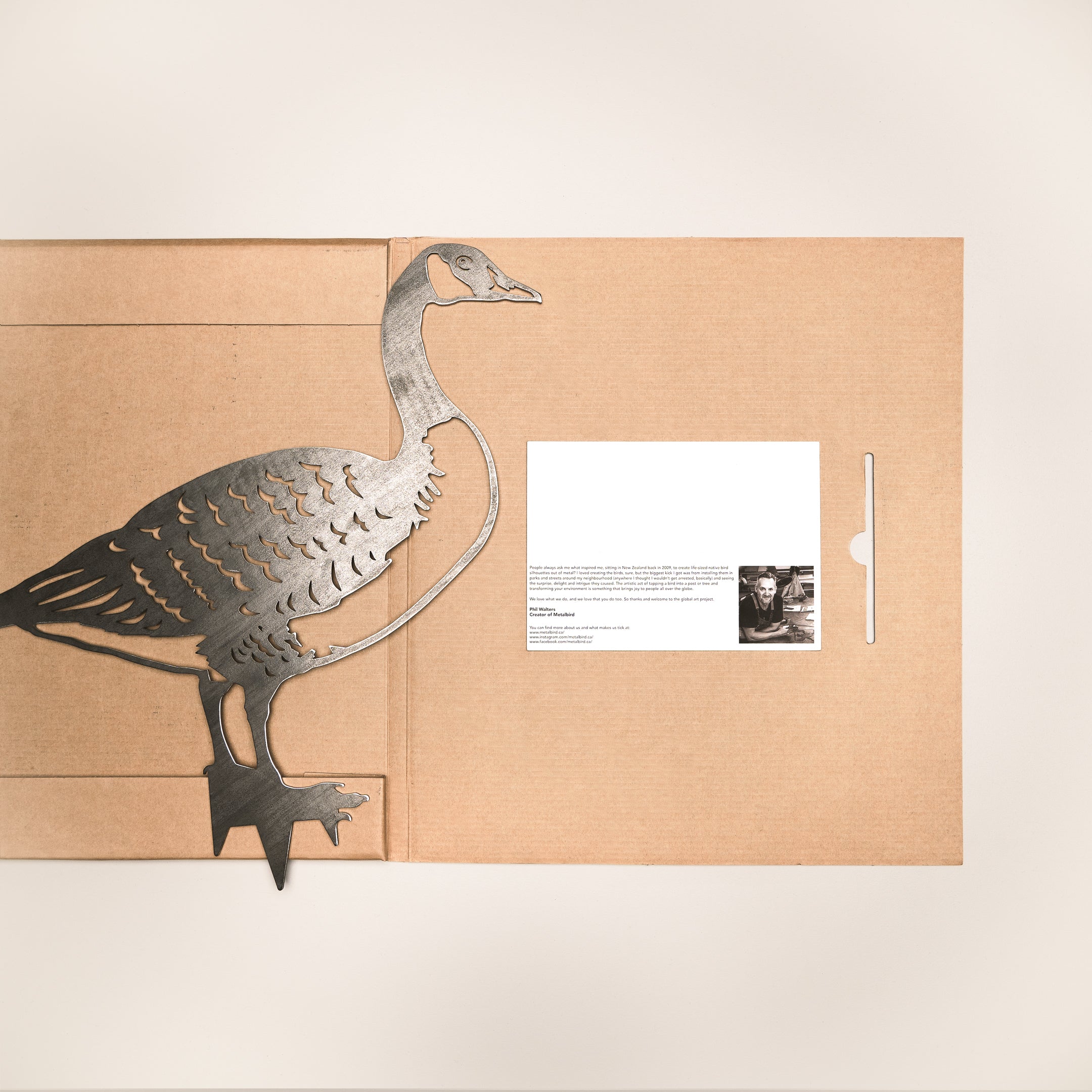 The Metalbird Canada "Canada Goose" is a metallic yard art piece, shown partly inside a brown folder next to a white card with text and black-and-white images, all set on a plain light background.