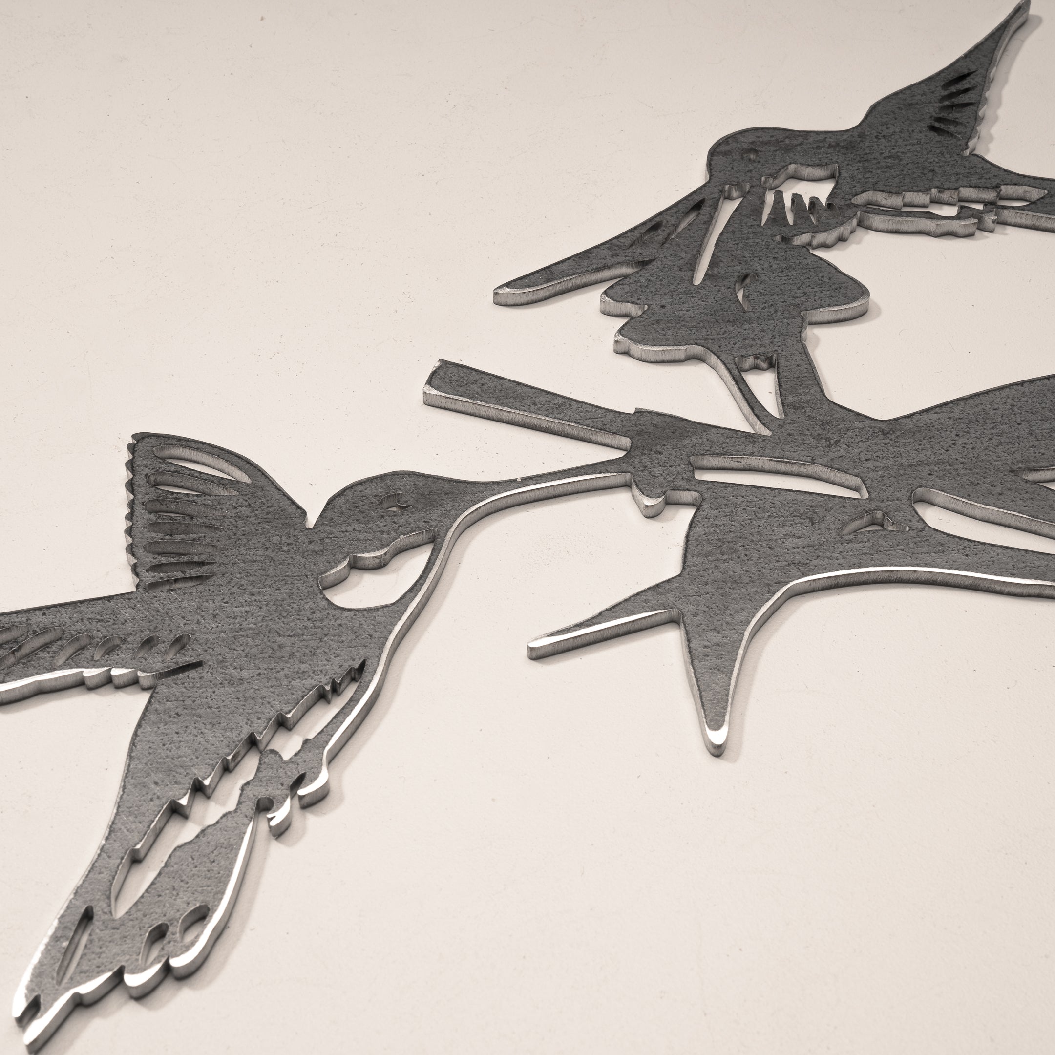 A close-up of Metalbird Canada’s Hummingbird Honeys, a metal garden art piece with two stylized hummingbirds perched on branches, featuring a smooth, reflective surface against a light background.