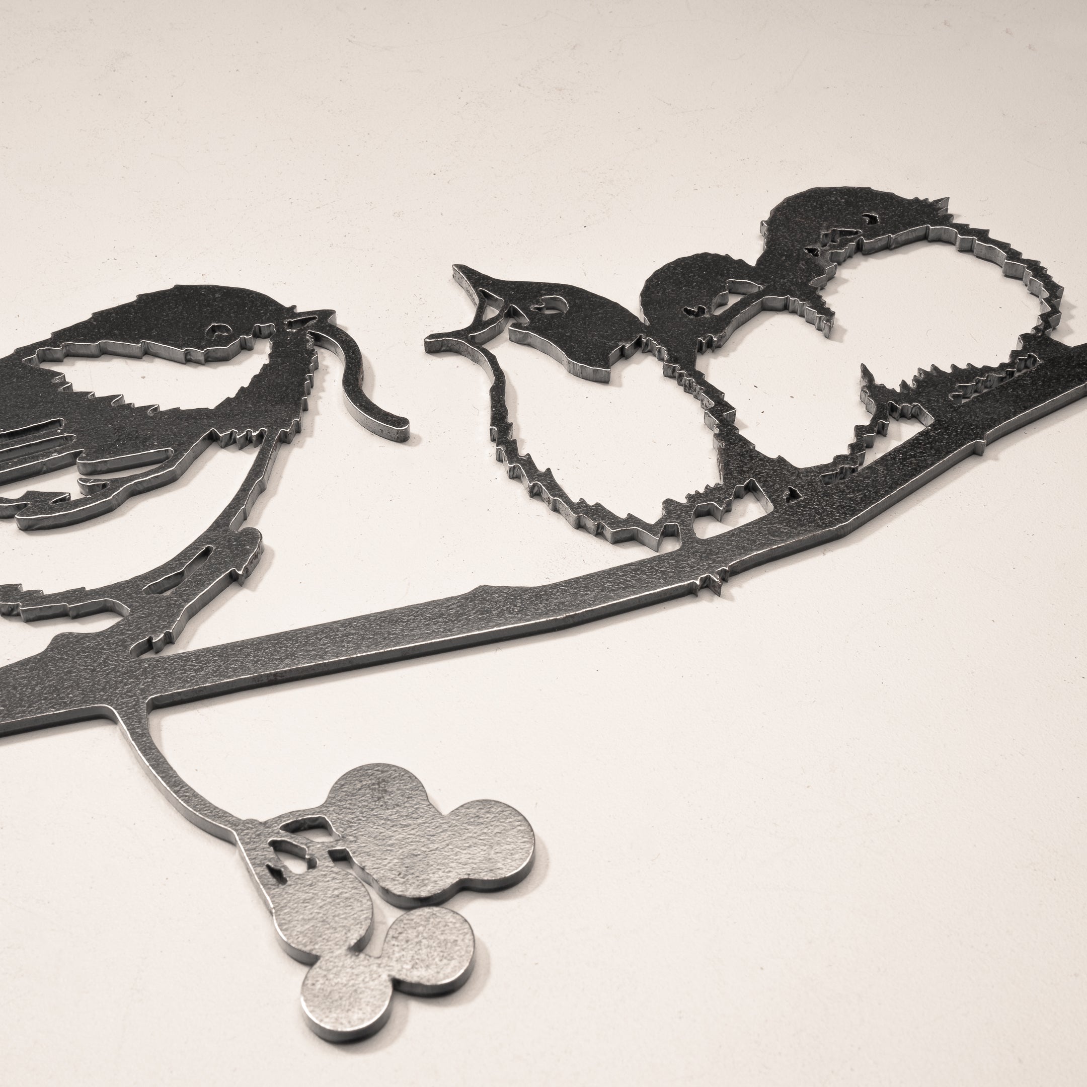 The Metalbird Canada "Chickadee & Chicks" black metal wall art features three birds on a leafy, berry-adorned branch—ideal as striking yard art or an elegant indoor accent.