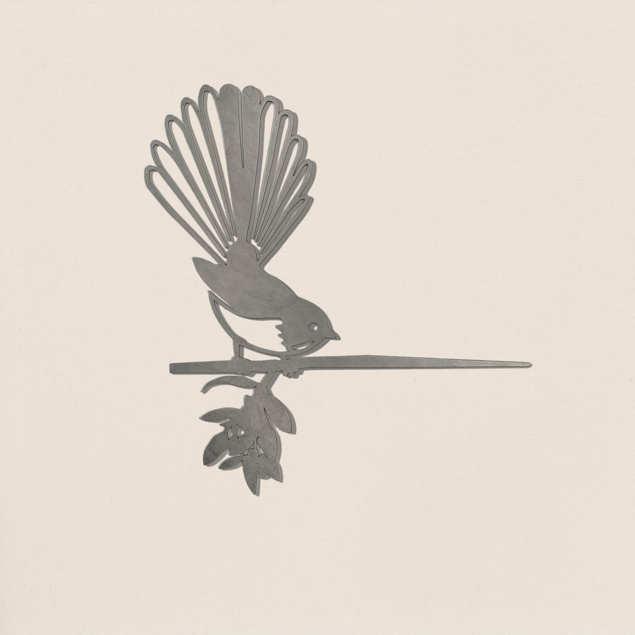 The Fantail / New Zealand Pīwakawaka by Metalbird Canada is a corten steel bird silhouette perched on a leafy branch with a flower, set against a light background—an ideal garden art piece or thoughtful gift.