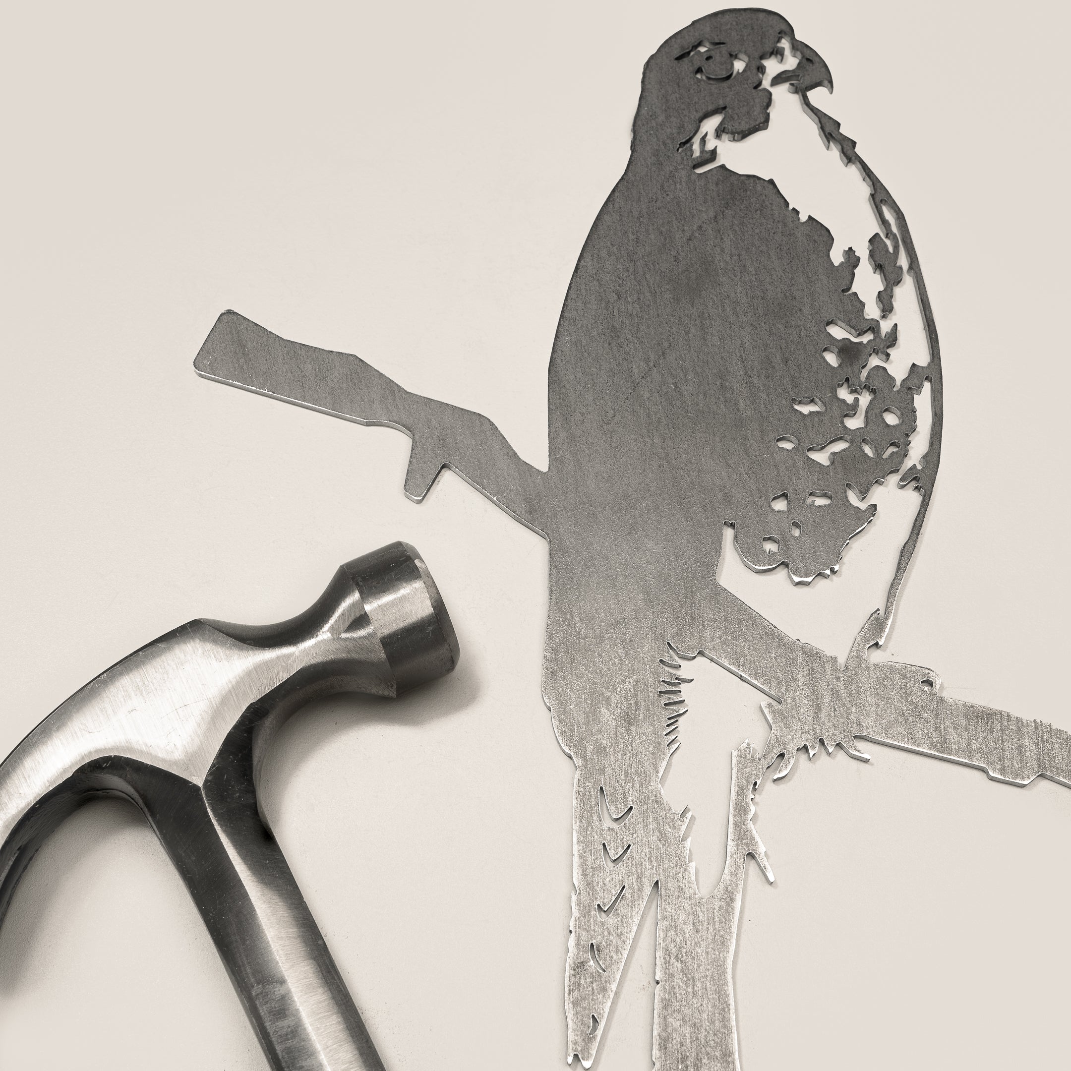 A silver hammer beside Metalbird Canada’s “Peregrine Falcon” corten steel silhouette, both set on a light surface—an ideal gift for nature lovers.
