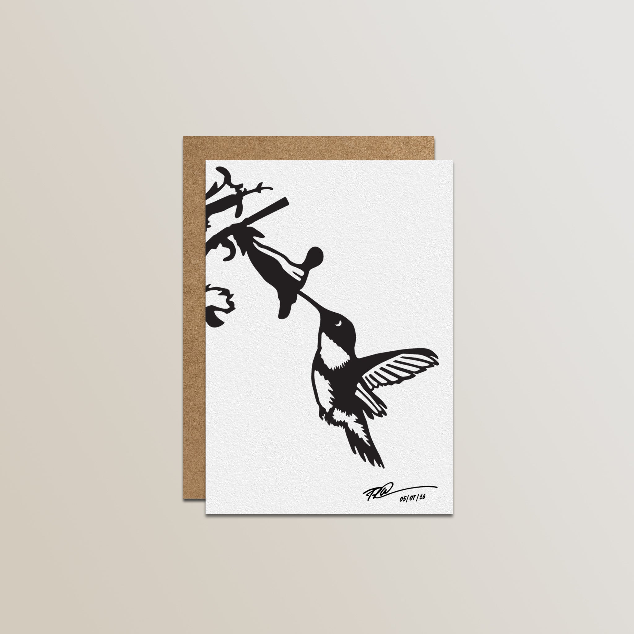 The Metalbird Canada Metalbird Greeting Card Set features a white card with a black silhouette hummingbird and flower design, inspired by metal yard art, paired with a brown envelope against a light backdrop.