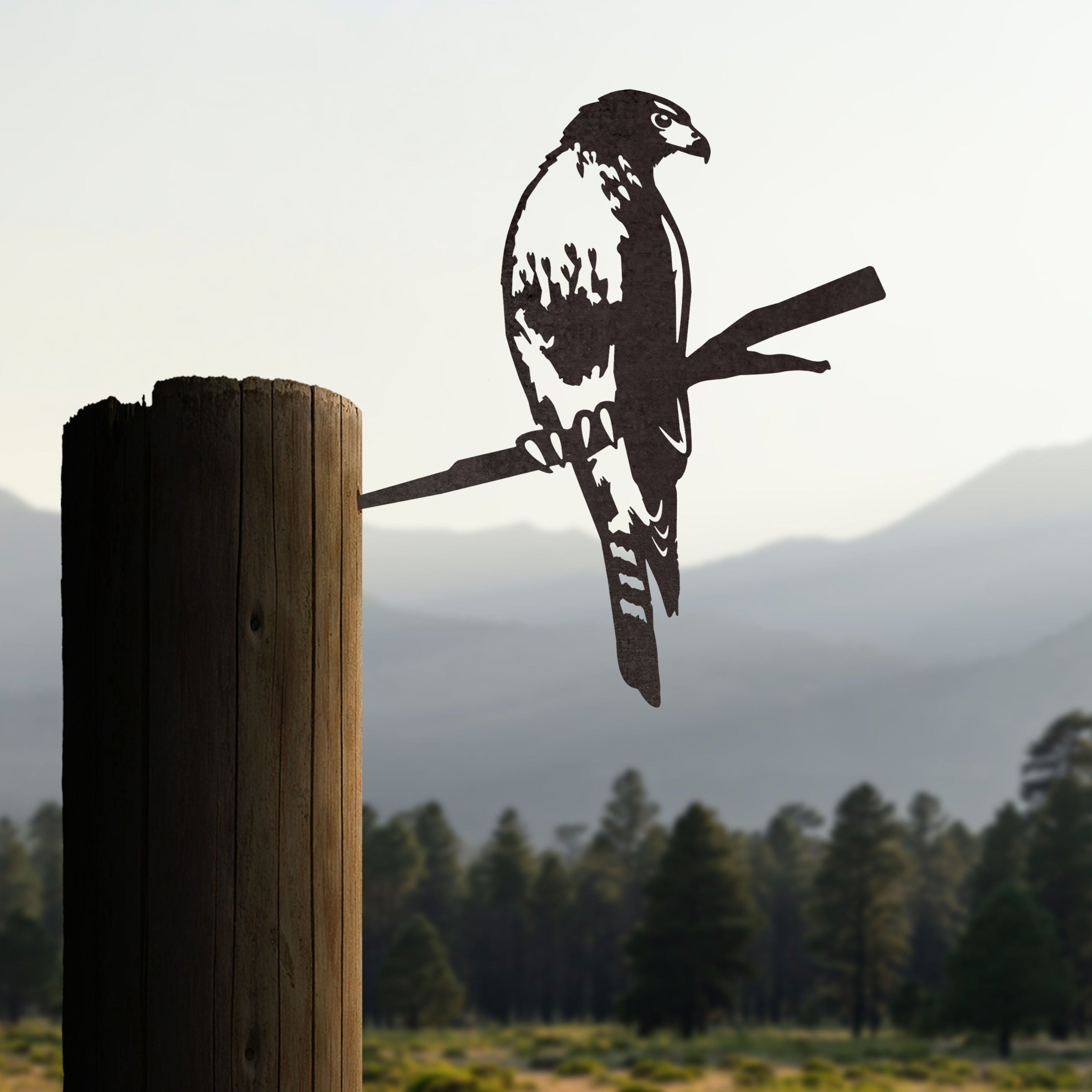 The Red-Tailed Hawk by Metalbird Canada is a corten steel bird silhouette perched on a post, creating striking yard art against natural scenery—an ideal gift for nature lovers.