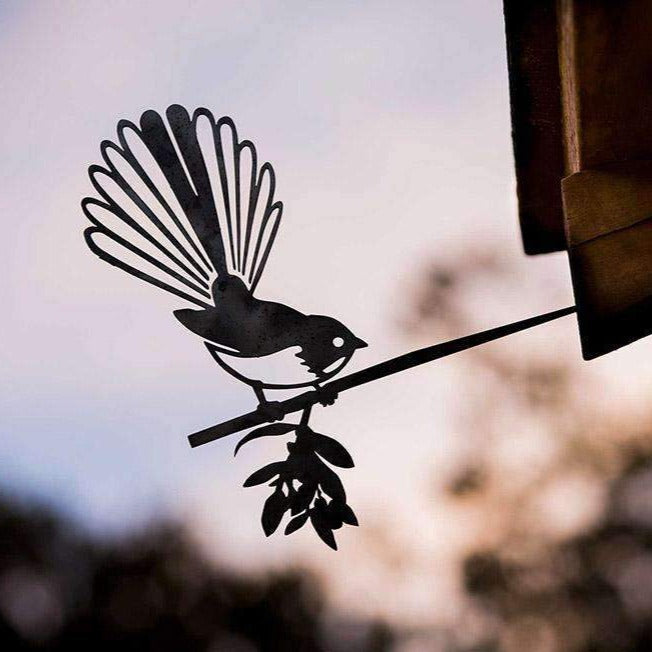 The Metalbird Canada Fantail / New Zealand Pīwakawaka is a corten steel bird silhouette with a fanned tail, perched on a leafy rod—an ideal gift for nature lovers, beautifully set against a softly blurred dusk sky.
