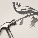 The Cardinal Mom & Mini Set by Metalbird Canada—a metallic hammer and a metal cutout of a cardinal on a branch—rests on a light surface, making it an ideal gift for bird lovers.