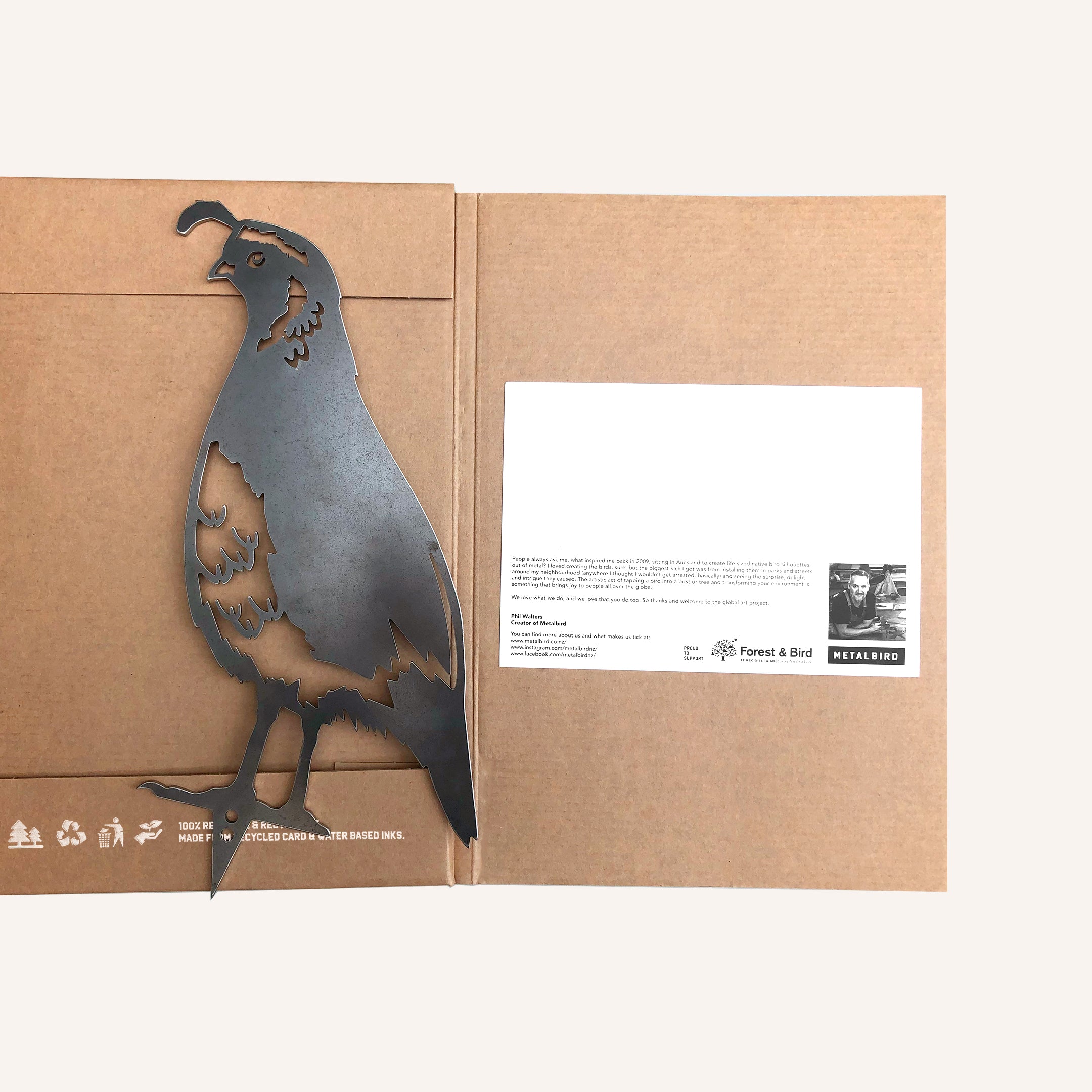 The Quail by Metalbird Canada is a metal bird silhouette attached to an open brown folder with a white info card, featuring text, logos, and a small black-and-white photo—makes a unique and charming garden art gift.