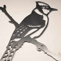 The MBPROMO Blue Jay ornament features cut-out patterns and geometric details in Corten steel, shaped like a bird perched on a branch. Ideal as Blue Jay garden decor or unique metal yard art. Photographed on a light background.