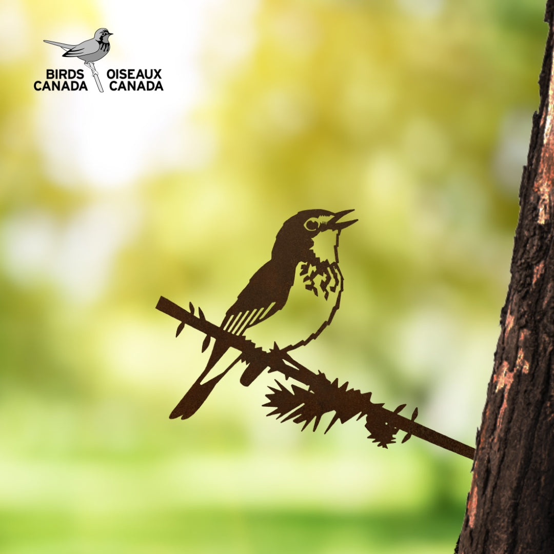 A Canada Warbler silhouette by Metalbird Canada perches on a branch attached to a tree trunk, serving as unique yard art with the Birds Canada logo and a blurred green background.