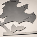 The Metalbird Canada Bat is a metal wall decor shaped like a bat with outstretched wings perched on a leafy branch—unique garden art shown on a plain white background.