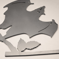 The Metalbird Canada Bat is a metal wall decor shaped like a bat with outstretched wings perched on a leafy branch—unique garden art shown on a plain white background.