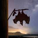 The Bat by Metalbird Canada hangs upside down from a branch on a wooden post—a striking metal garden art piece that's perfect for any outdoor space.