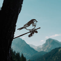 The Magnolia Warbler by Metalbird Canada is a corten steel bird silhouette perched on a branch, attached to a tree trunk for unique garden art.