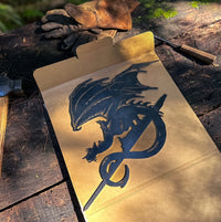 The FELL BEAST™ by Metalbird Canada is a black metal dragon silhouette with wings and a curled tail, resting on an open box beside tools—perfect as eye-catching garden or yard art for your outdoor space.