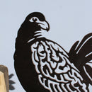 A close-up of the Manumea metal bird silhouette by Metalbird Canada - CC, featuring intricate feather details. This unique garden art is mounted on a wooden base and set against a plain, light-colored background.