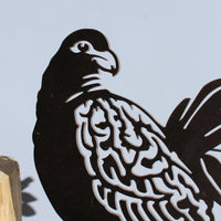 A close-up of the Manumea metal bird silhouette by Metalbird Canada - CC, featuring intricate feather details. This unique garden art is mounted on a wooden base and set against a plain, light-colored background.