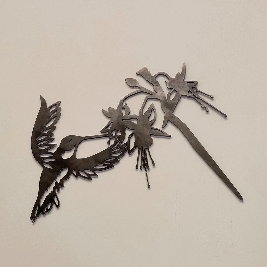 The Metalbird Canada Ruby-Throated Hummingbird is a handcrafted metal wall art sculpture featuring a hummingbird feeding from fuchsia flowers, designed with cutout details—perfect bird decor for bright, light-colored walls.