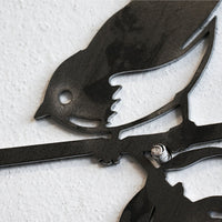 A close-up of Metalbird Seconds by Metalbird Canada - Seconds, a black corten steel wall art shaped like a bird on a branch, mounted on a textured white wall—an ideal unique gift.
