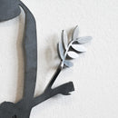 A close-up of the Metalbird Seconds by Metalbird Canada - Seconds shows a corten steel wall art piece featuring part of a branch with flat, oval leaves, creating an elegant silhouette against a light textured wall.