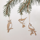 Wooden Hanging Decorations by Metalbird Canada feature an owl, a songbird, and a cardinal silhouettes dangling from a pine branch—unique accents for garden art or home décor.