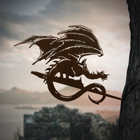 Mounted on a tree, the FELL BEAST™ metal silhouette by Metalbird Canada features outstretched wings, creating dramatic yard art against a backdrop of hills, water, and ancient ruins.