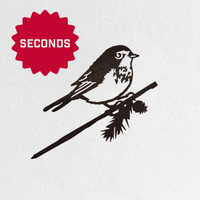 Metalbird Seconds by Metalbird Canada - Seconds: black metal silhouette of a small bird on a pine branch, with a red "SECONDS" starburst in the top left, all set against a textured white background—an eye-catching, unique gift.