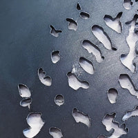 Close-up of Metalbird Seconds by Metalbird Canada - Seconds: a dark metal surface with organic-shaped cutouts revealing lighter material below. The smooth, rounded edges create a striking silhouette reminiscent of modern yard art.