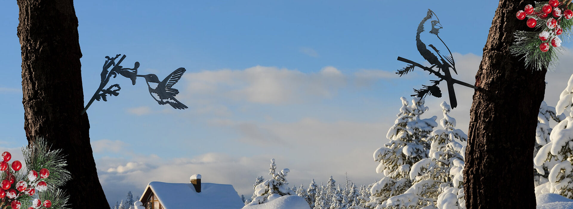 Decorative metal birds on trees with a snowy landscape and cabin in the background