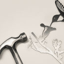 A metal hammer rests beside Metalbird Canada’s "Hummingbird," a corten steel silhouette of a bird, branch, and flower—unique garden art accents—displayed on a light background.