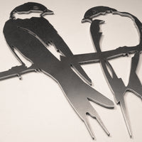 The Pair of Swallows by Metalbird Canada features two stylized birds perched on a branch. Made from corten steel, this metal garden art showcases sharp edges and minimal detailing for a modern outdoor display.
