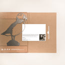 The Metalbird Canada Puffin comes in eco-friendly cardboard packaging featuring a puffin silhouette, white icons, and text. An inserted white card with text and a black-and-white photo makes it ideal for unique garden art lovers.