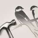 A silver hammer rests beside Metalbird Canada's "Pair of Swallows" metal bird silhouettes perched on a branch, all set against a light background—a thoughtful gift for any occasion.