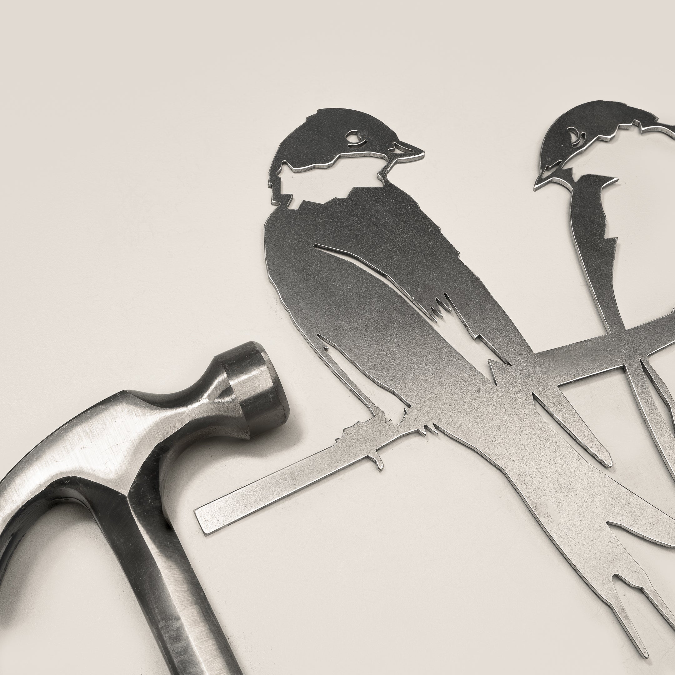 A silver hammer rests beside Metalbird Canada's "Pair of Swallows" metal bird silhouettes perched on a branch, all set against a light background—a thoughtful gift for any occasion.