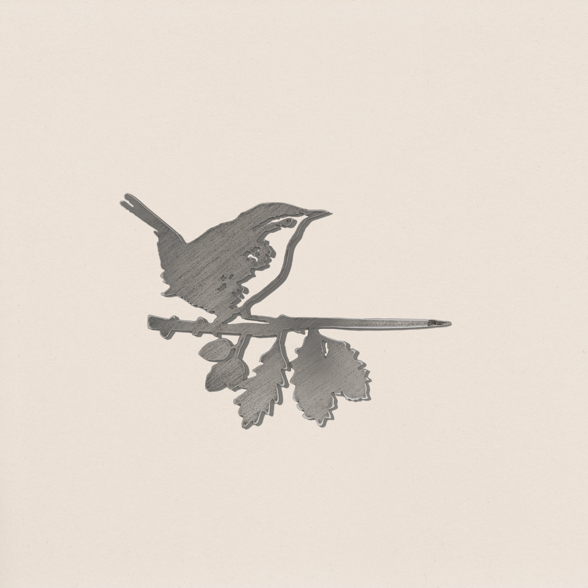 The Wren by Metalbird Canada is a corten steel silhouette of a small bird on a leafy branch, set against a light beige backdrop—ideal as charming yard art.