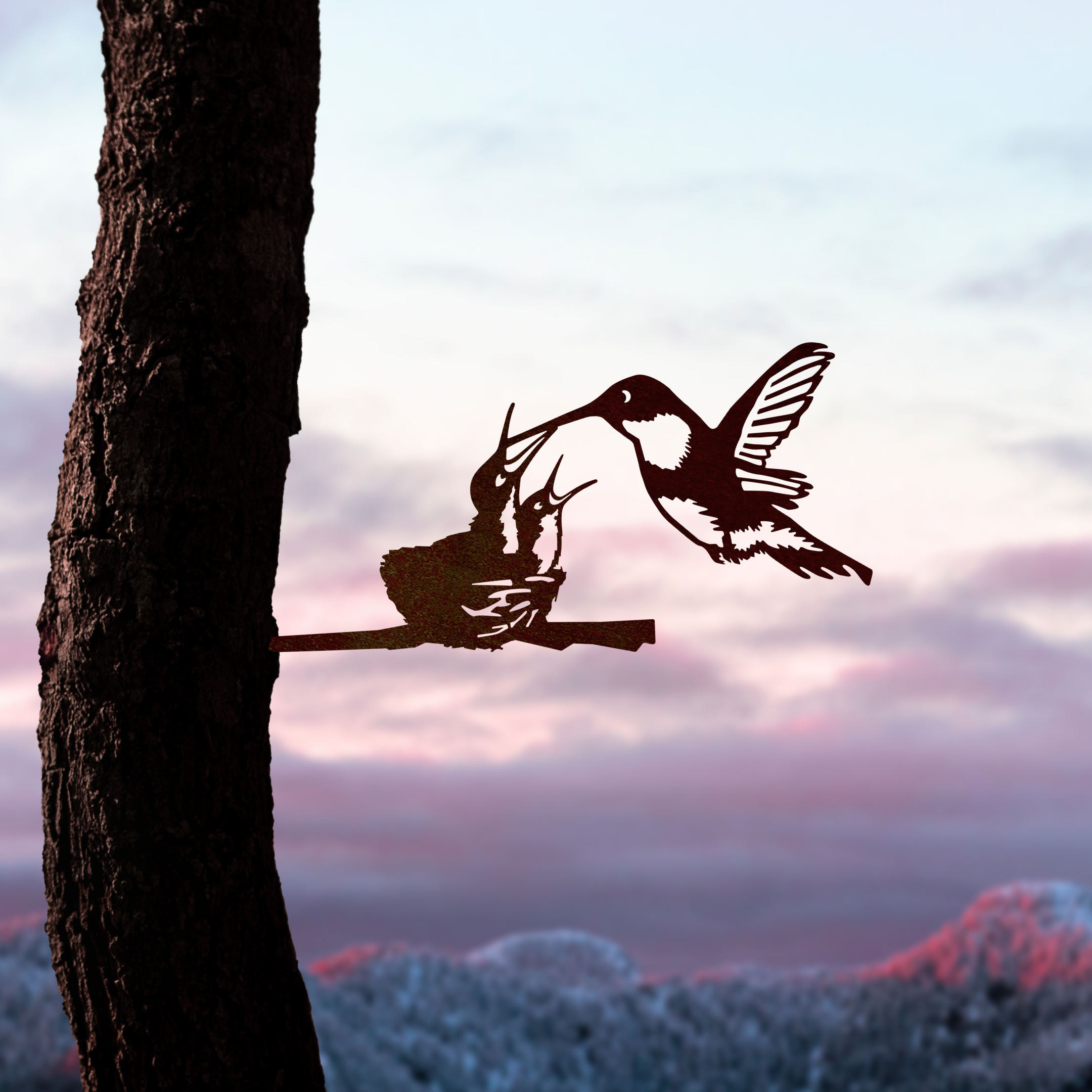 A silhouette of Metalbird Canada's Hummingbird & Chicks, featuring a hummingbird feeding chicks in a nest on a branch against a vibrant sky and mountains—an ideal Mother's Day gift.