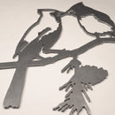 Kissing Cardinals by Metalbird Canada is metal wall art crafted from corten steel, featuring two birds perched on a branch with pine needles in a minimalist silhouette style.