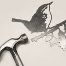 The Wren by Metalbird Canada is a delicate corten steel cutout of a bird perched on a leafy branch, shown beside a metal hammer against a light background—a charming piece of yard art.
