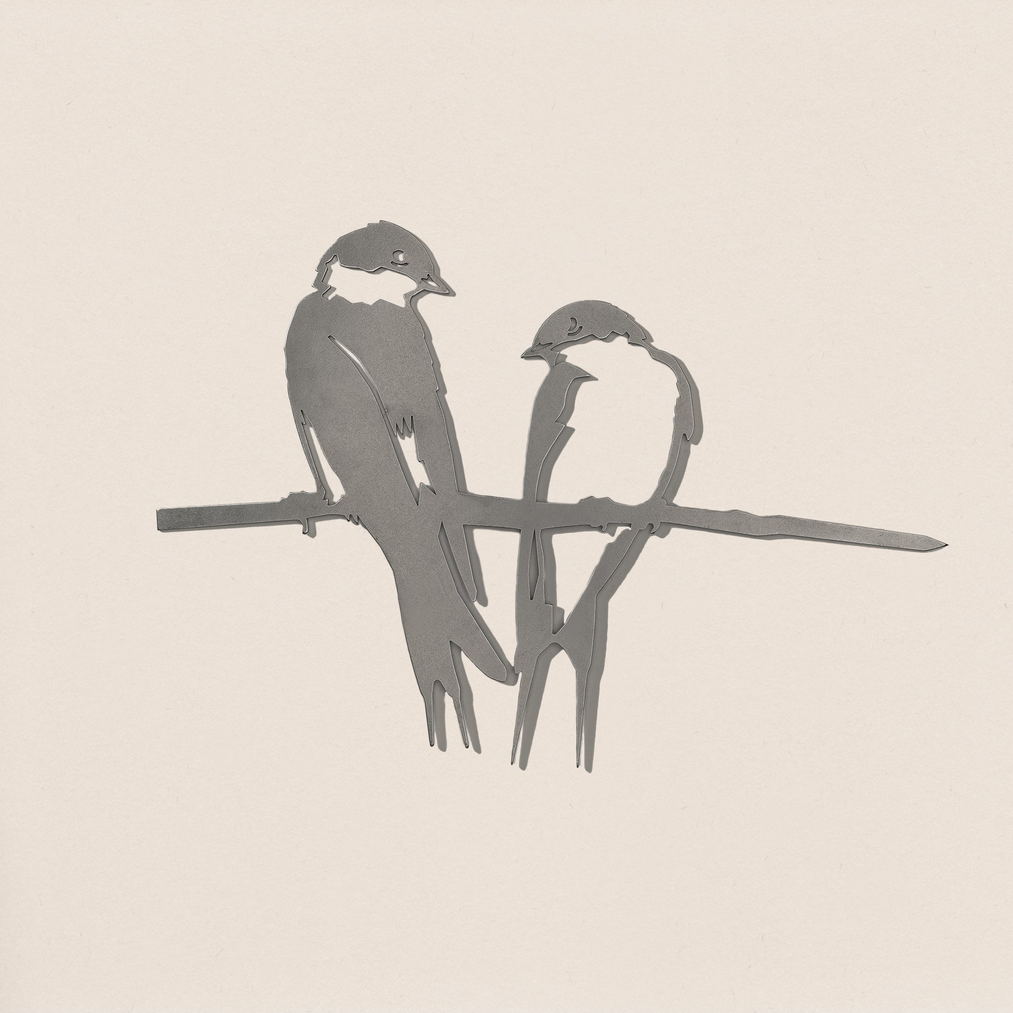 The Pair of Swallows by Metalbird Canada features two minimalist swallows perched closely together, crafted in striking grayscale metal silhouette—a modern garden art piece set against a clean, light backdrop.