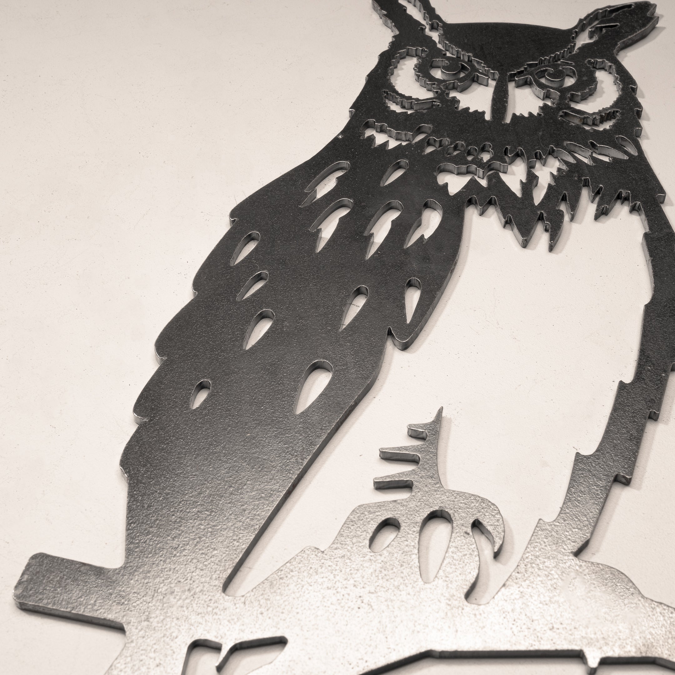 The Great Horned Owl by Metalbird Canada features intricate metal cutouts with detailed feathers and piercing eyes, perched on a branch against a plain, light background—an eye-catching piece of metal garden art.
