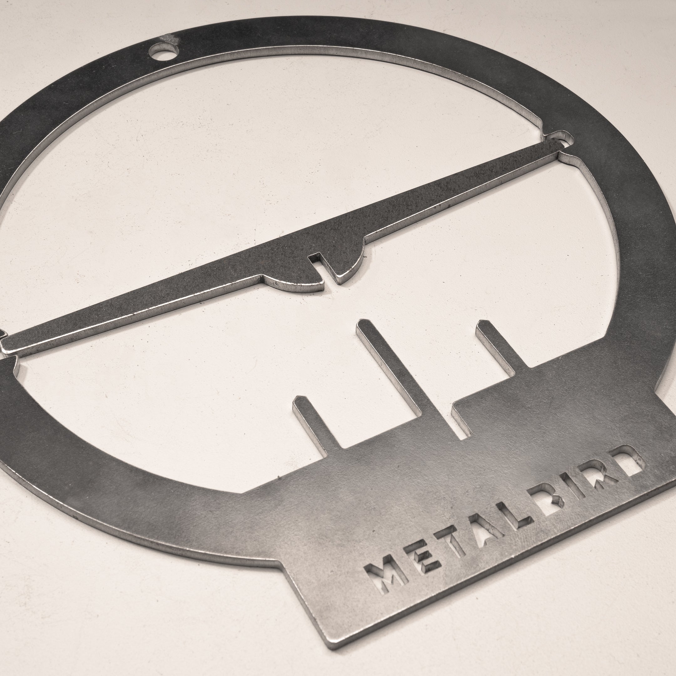 The Hanging Bird Feeder by Metalbird Canada features a corten steel bird design with a circular frame and horizontal bar, engraved “METALBIRD” at the base—perfect as unique yard art or a thoughtful gift, shown on a light surface.