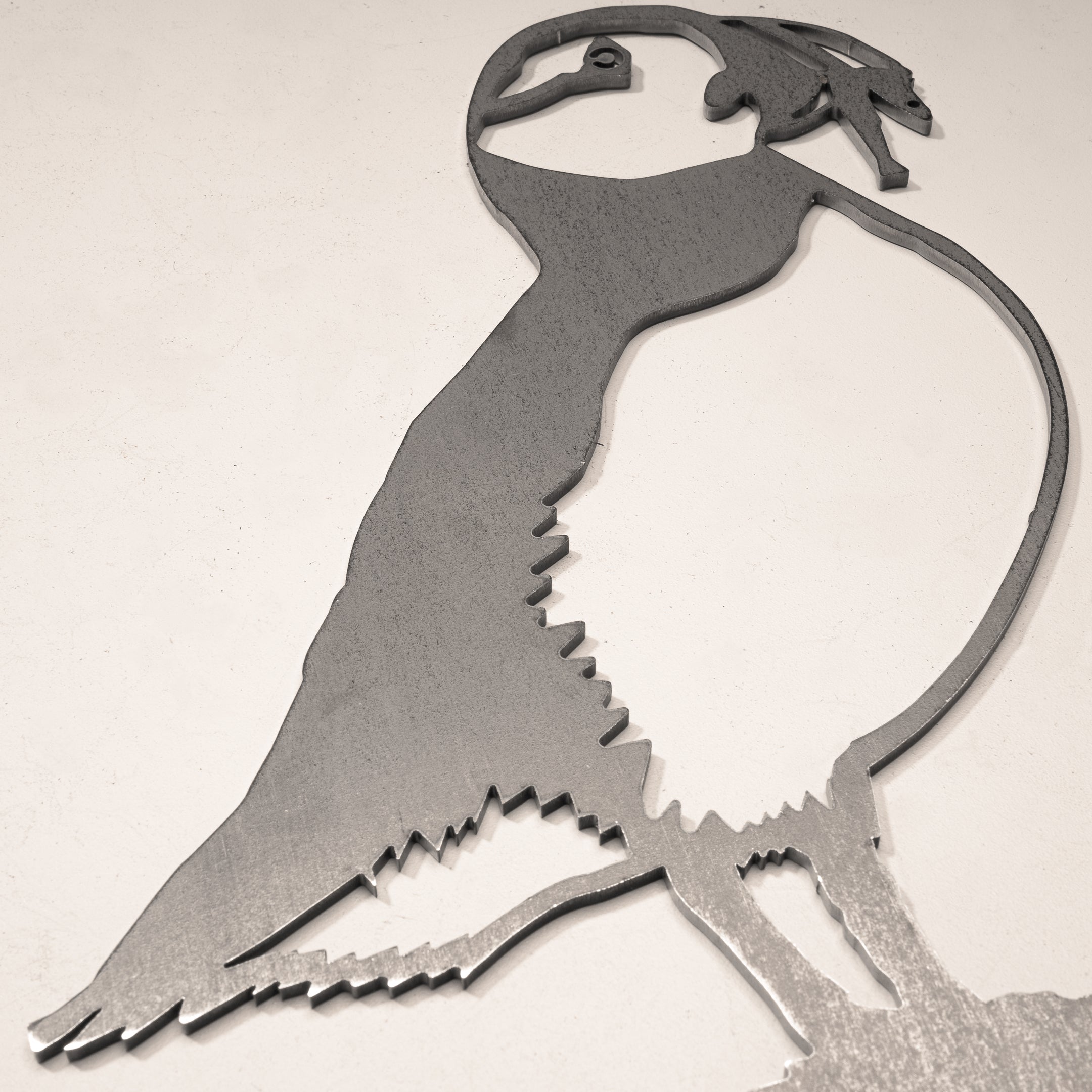 The Metalbird Canada Puffin is a corten steel silhouette of a puffin, mounted on a light-colored wall. It features simple, stylized lines with minimal detail for a modern look.