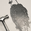 A metal hammer rests beside Metalbird Canada's Bald Eagle—a flat, intricately cut corten steel piece shaped like an eagle on a branch—ideal as unique garden art or a thoughtful gift, both set on a light surface.