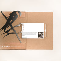 Pair of Swallows by Metalbird Canada: A brown cardboard folder with black bird silhouettes, ideal as a gift. The partially open folder reveals a white card with text and a black-and-white photo. Environmental and recycling icons shown bottom left.