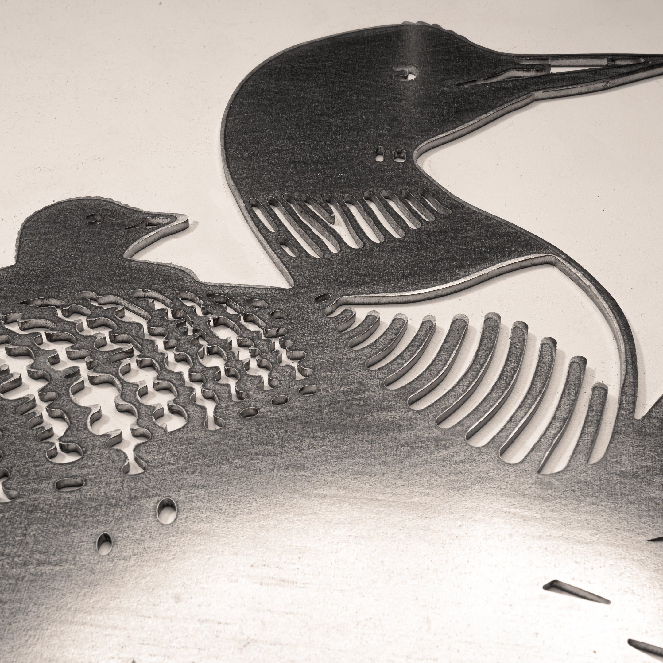 The Metalbird Canada "Common Loon" features laser-cut metal silhouettes of two loons, one larger and one smaller, with detailed feathers—an elegant, reflective piece perfect for any nature lover.