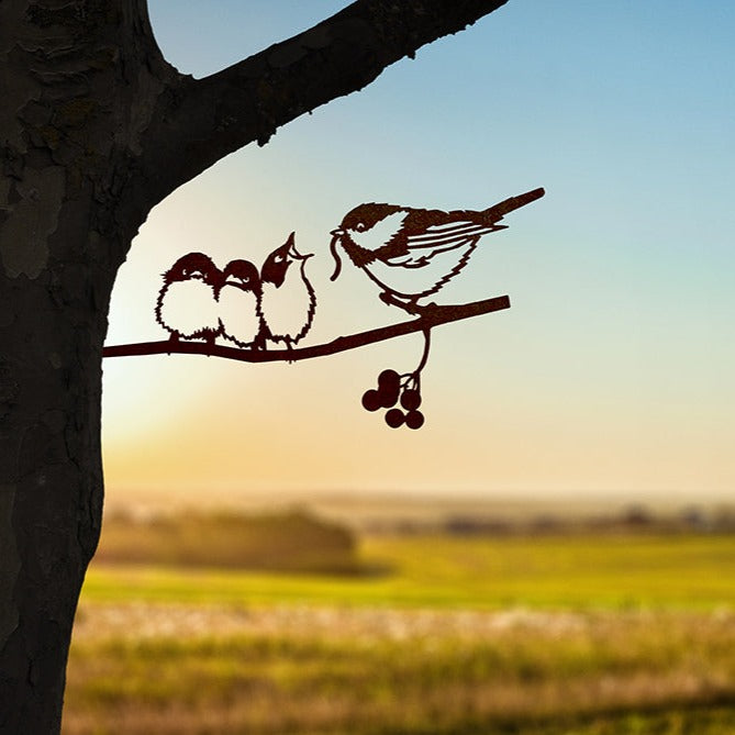 Chickadee and two chicks steel silhouette mounted on a tree above a sunlit field.