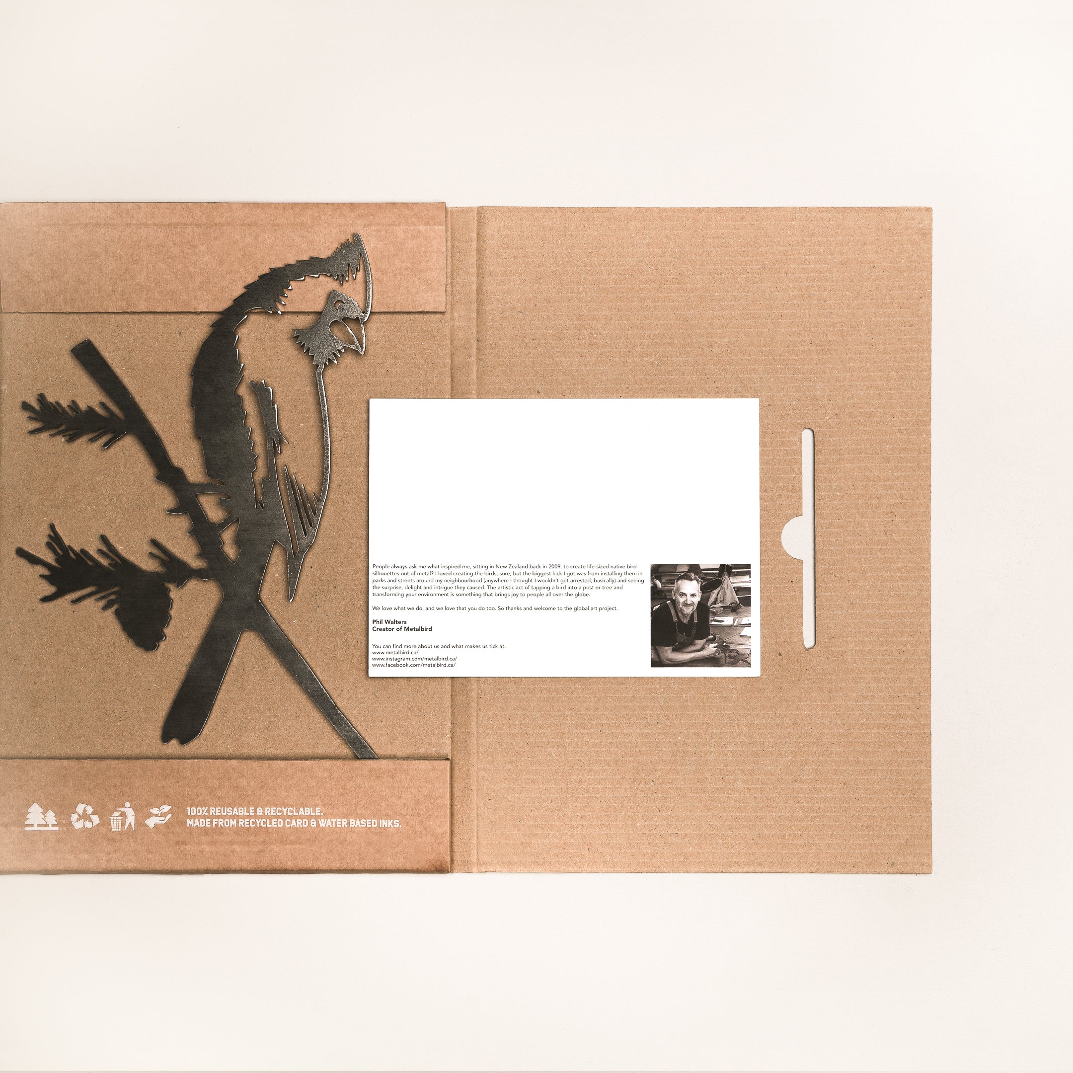 The Cardinal by Metalbird Canada features a brown cardboard folder with a bird-on-branch cutout on the left and a white card with text and a black-and-white photo on the right, partially tucked into a slot.